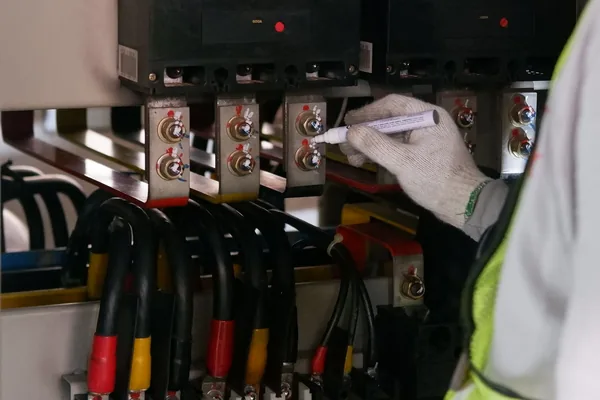 A gloved hand marking bolted cable connections below large molded-case breakers
