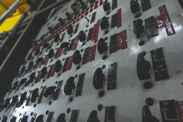 An old control panel with rows of rotary switches and engraved circuit labels