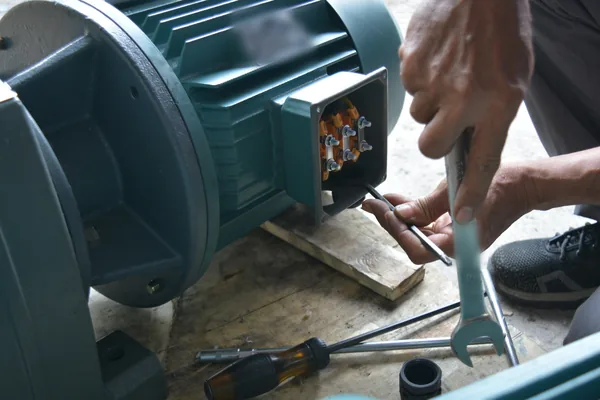 Hands wiring the terminal box of a three-phase motor with a wrench and nut driver