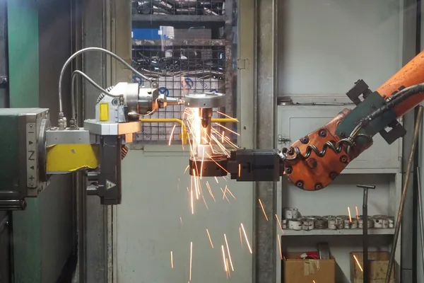 A robot arm and positioner working in a welding cell, with sparks flying