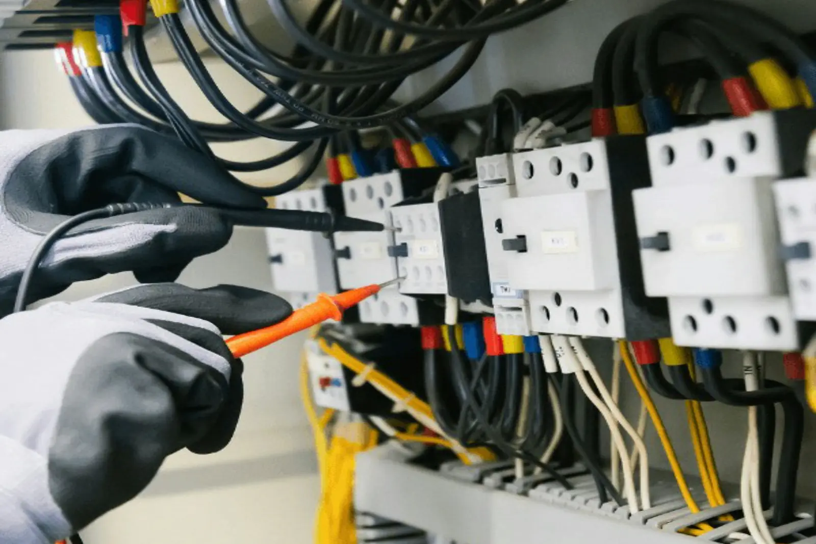 Gloved hands testing a motor control panel with a multimeter