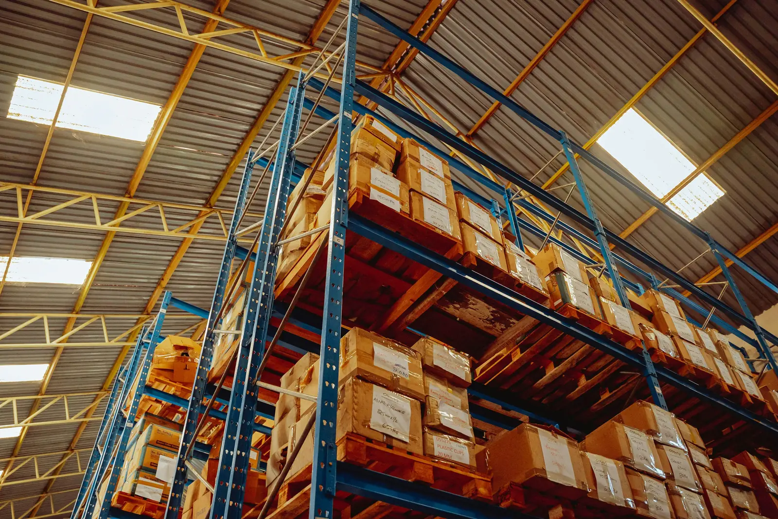 Tall blue pallet racking loaded with cartons under a steel roof